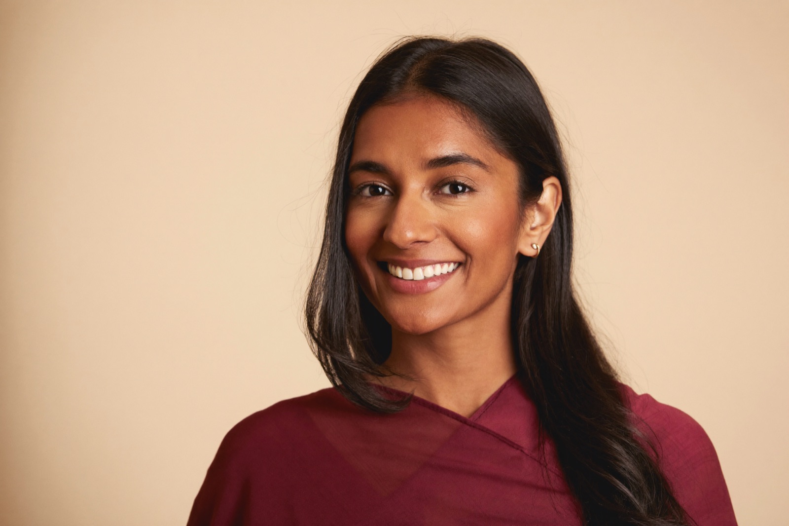 An ideal Shaadi.com profile photo: a woman in a solid maroon saree, head-and-shoulders framing, a warm natural smile, against a plain cream background